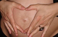 Hände formen ein Herz auf einem Babybauch